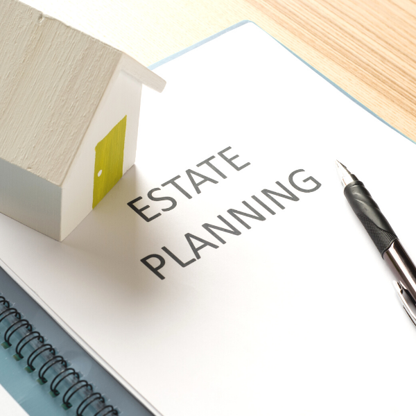 Black pen laying on top of a packet titled Estate Planning that contains estate plan documents planning for certainties in life, death and taxes, with a miniature house sitting on top.